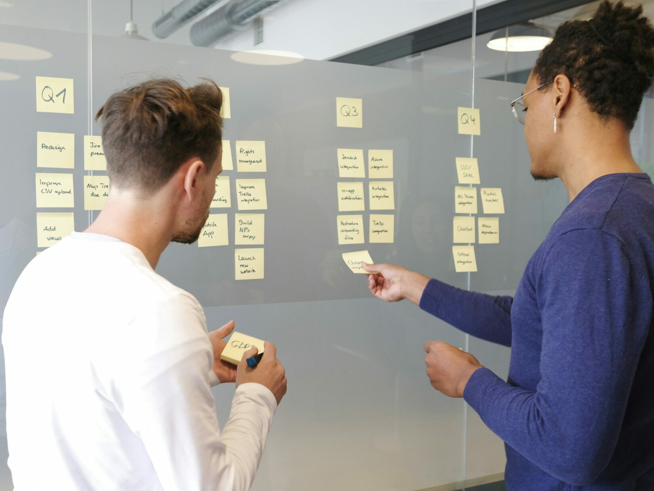 deux hommes posent des post il sur un tableau transparent