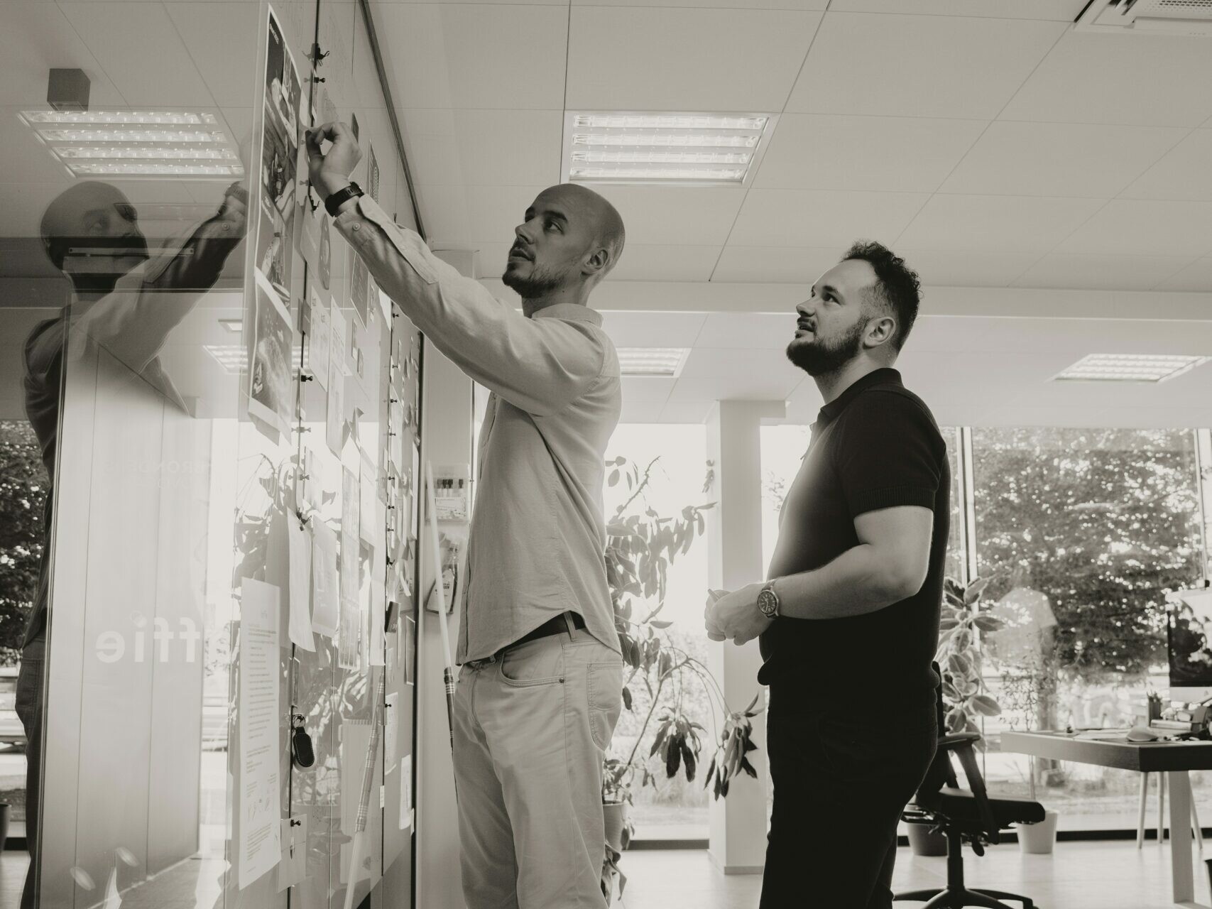 Deux hommes debout l’un à côté de l’autre en face d'un tableau blanc