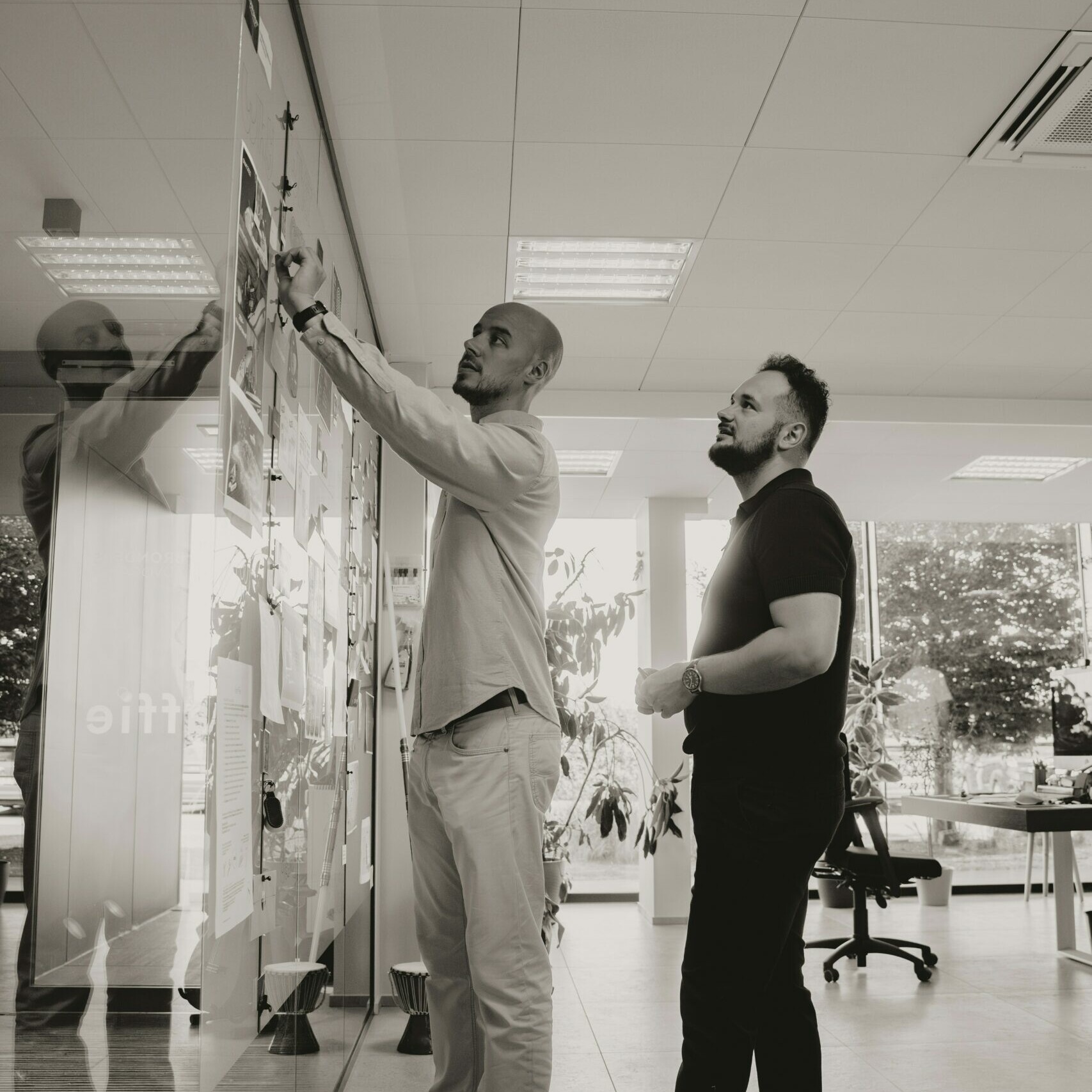 Deux hommes debout l’un à côté de l’autre en face d'un tableau blanc